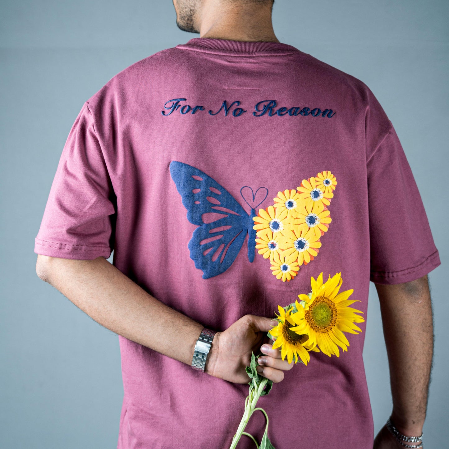 Back view of WHIMSICAL WINGS MAUVE T-SHIRT showcasing embroidered butterfly and sunflower design in purple.