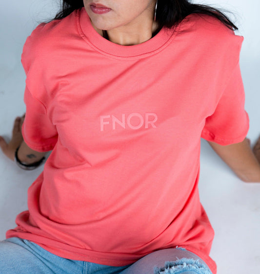 A person sitting down in the FNOR PIGLET SANDWICH T-SHIRT, showcasing the subtle front FNOR logo in light print.