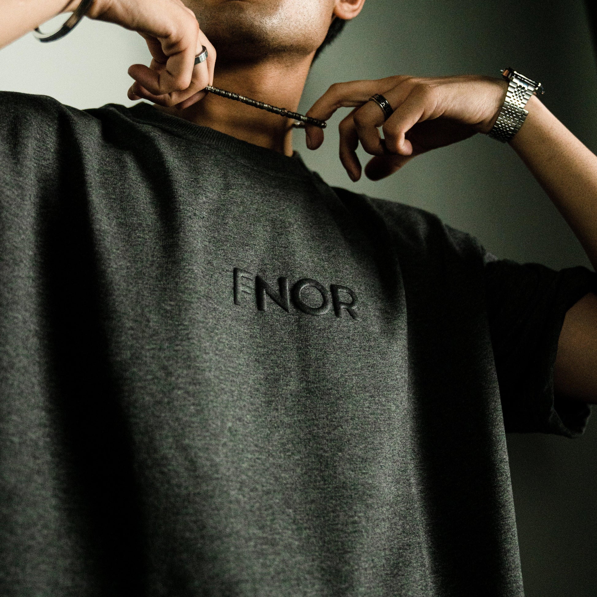 Close-up of a person wearing the STONED ASH GREY T-SHIRT by FNOR, showcasing the subtle “FNOR” logo on the front in black puff print.