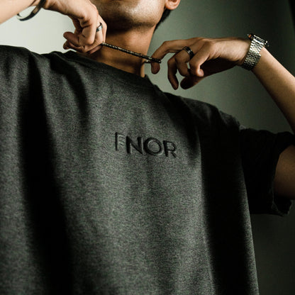Close-up of a person wearing the STONED ASH GREY T-SHIRT by FNOR, showcasing the subtle “FNOR” logo on the front in black puff print.