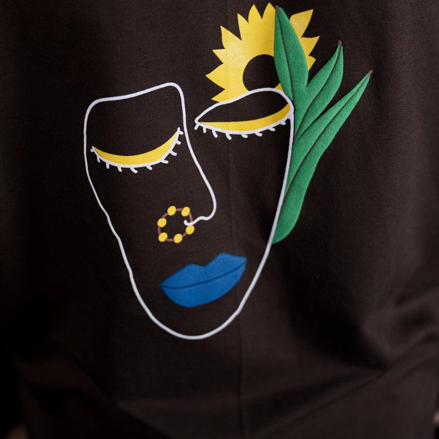 Close-up of the tribal face illustration on the back of the TRIBAL GANGSTER BROWN T-SHIRT by FNOR, showcasing vibrant colors and artistic details.
